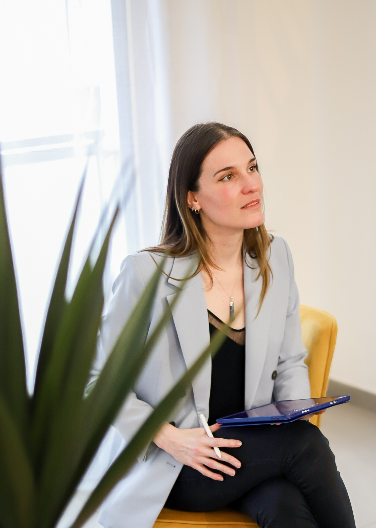 Photo de Vanessa Adis portant un blazer bleu clair, en consultation assise sur un fauteuil, tablette et stylet à la main, écoutant activement sa consultante